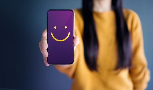 Mulher segurando celular com emoji de felicidade na tela.