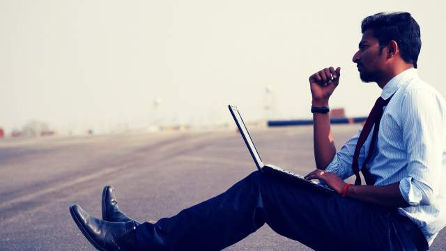 A man sitting by the roadside using his laptop