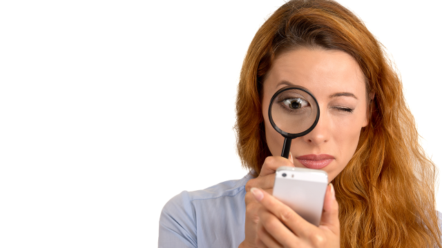 A woman looking at her smartphone through magnifying glass