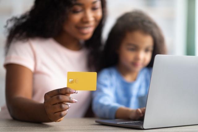 Online shopping. African American mother holding credit card, making purchases on web with her daughter, using laptop