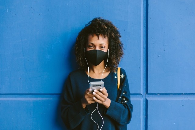 Stylish urban woman wearing face mask and texting on smartphone