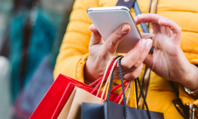 Mulher segurando celular com sacolas de compras na mão
